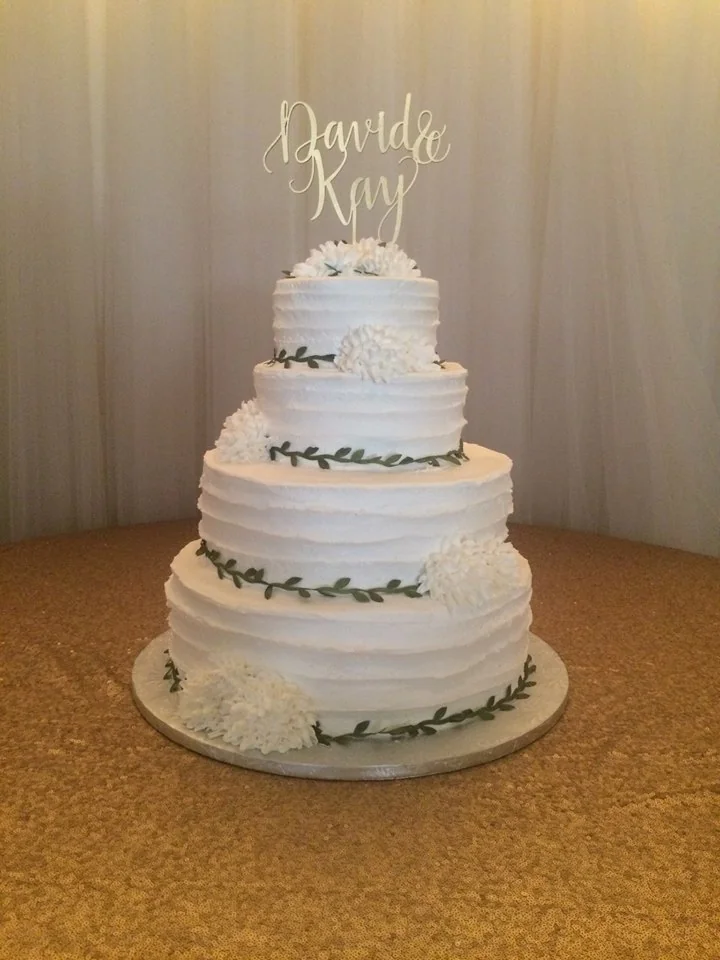 A tiered white celebration cake decorated with greenery