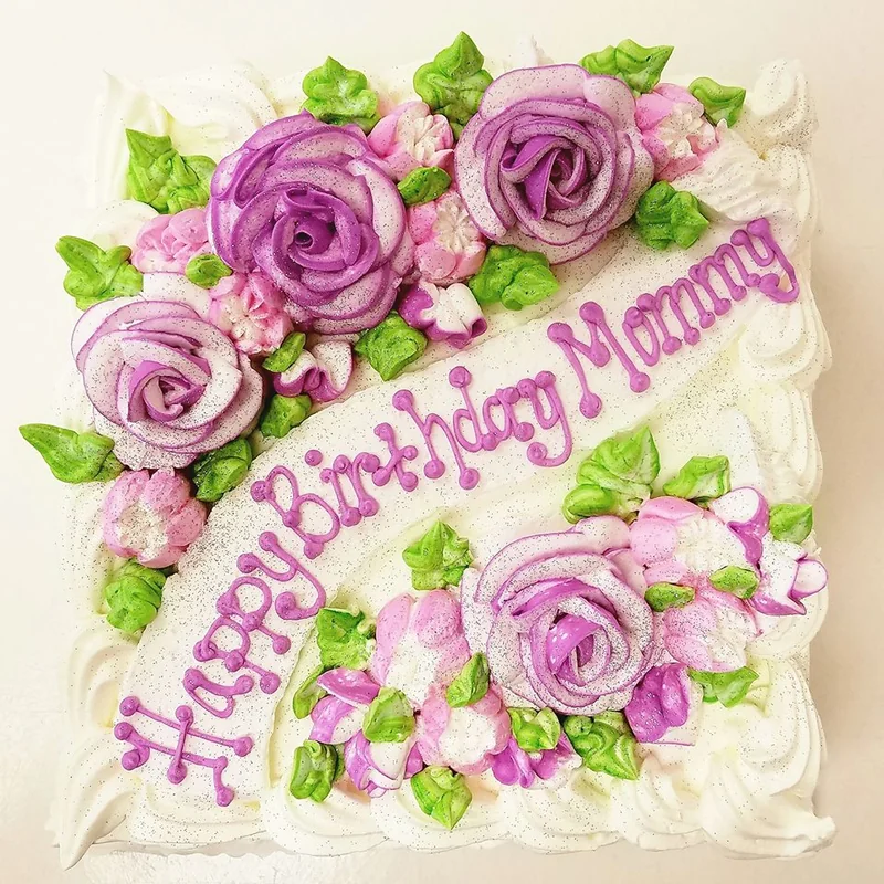 A white celebration cake decorated with purple icing roses