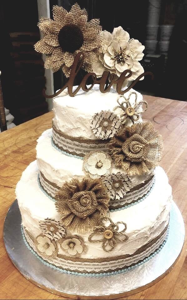 Three-tier cake decorated with burlap flowers, lace bands and a love topper
