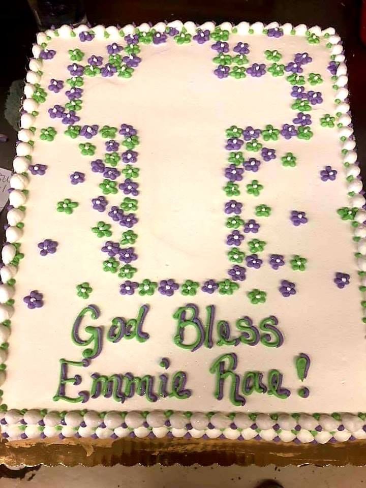 White sheet cake with a cross outlined in purple and green icing flowers
