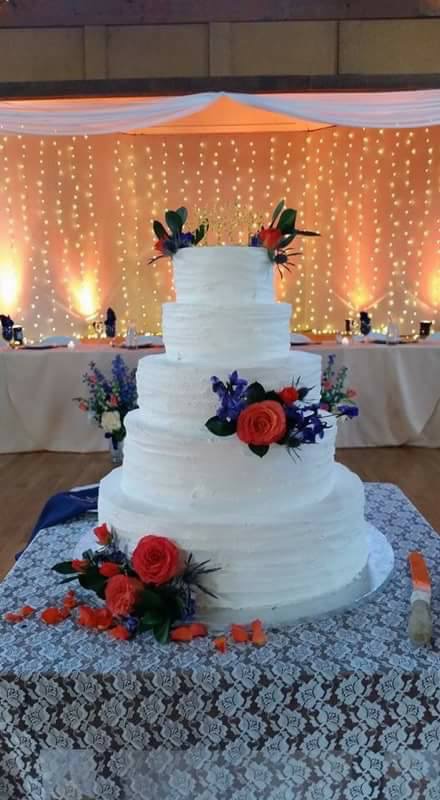 Tiered white wedding cake decorated with red roses and blue flowers